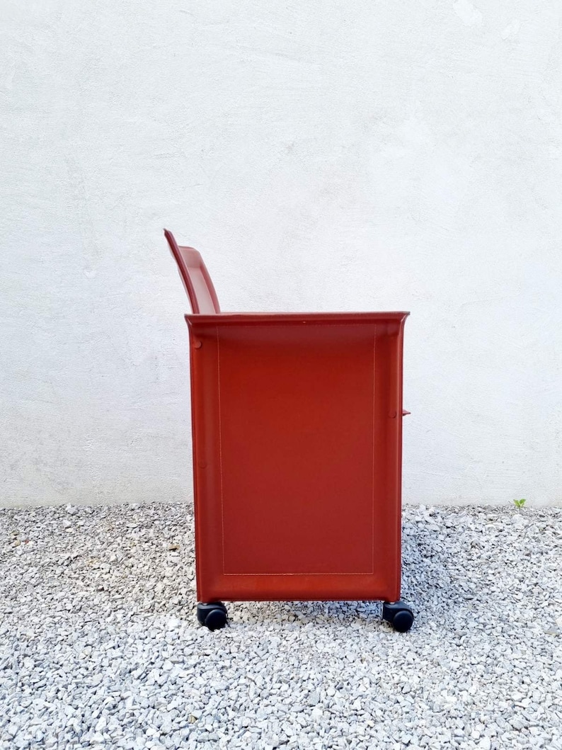 May include: A red rolling cabinet with three drawers and black wheels. The cabinet is made of metal and has a sleek, modern design.