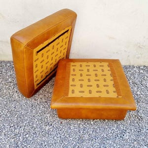 May include: Two-piece set of vintage furniture, featuring a square ottoman and a matching backrest. Both pieces are upholstered in tan leather with a patterned fabric insert. The ottoman measures approximately 18 inches square.