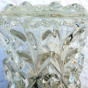 May include: A clear glass vase with a textured, geometric design. The vase has a wide mouth and a narrow base.