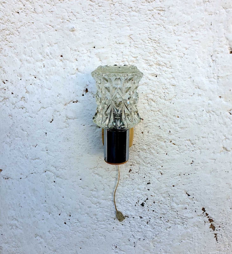 May include: A vintage wall sconce with a clear glass shade featuring a diamond pattern. The sconce has a chrome finish and a gold base.