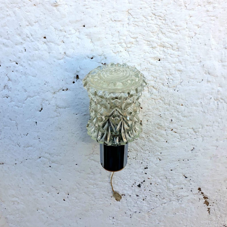 May include: A clear glass lampshade with a textured diamond pattern. The lampshade is attached to a black metal base with a cord hanging down.