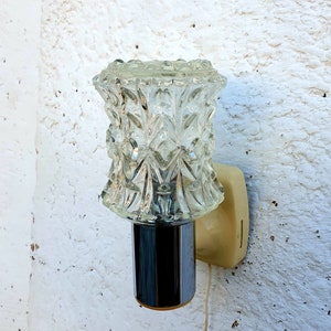 May include: A vintage wall sconce with a clear glass shade featuring a geometric pattern. The sconce has a chrome finish and a white plastic base.