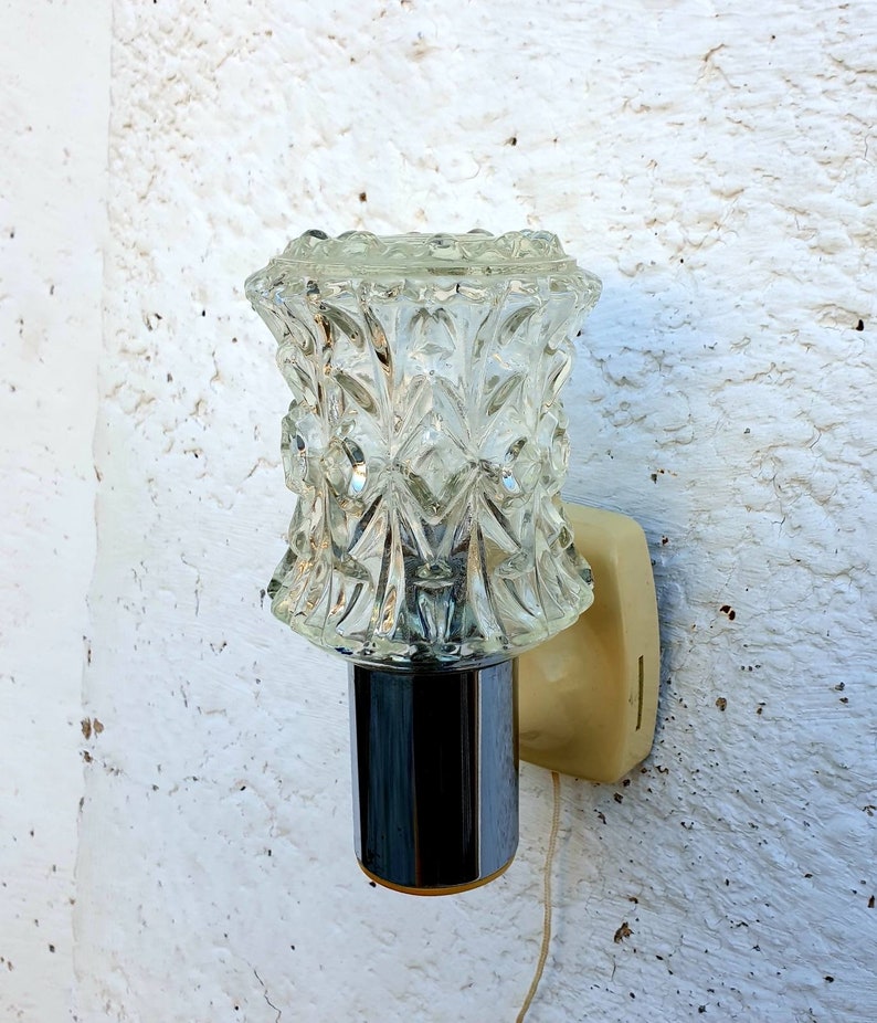 May include: A vintage wall sconce with a clear glass shade featuring a geometric pattern. The sconce has a chrome finish and a white plastic base.