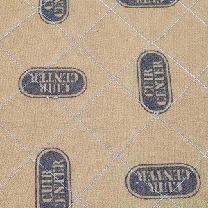 May include: Tan quilted fabric with a diamond pattern. The fabric is stamped with the words "CUIR CENTER" in a dark blue oval. The pattern is repeated across the surface.
