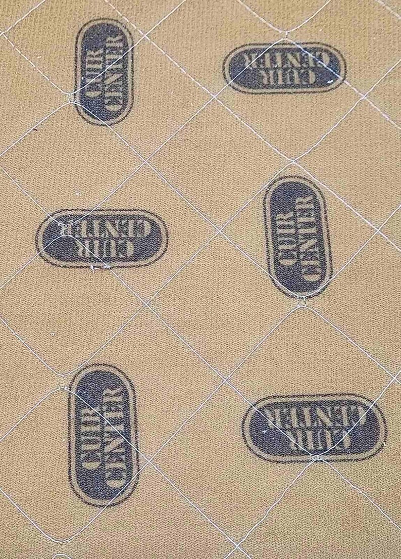May include: Tan quilted fabric with a diamond pattern. The fabric is stamped with the words "CUIR CENTER" in a dark blue oval. The pattern is repeated across the surface.