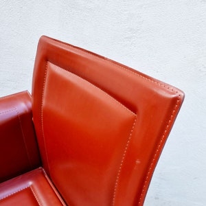 May include: Close-up of a red leather chair with a stitched design. The chair has a high back and a curved seat.