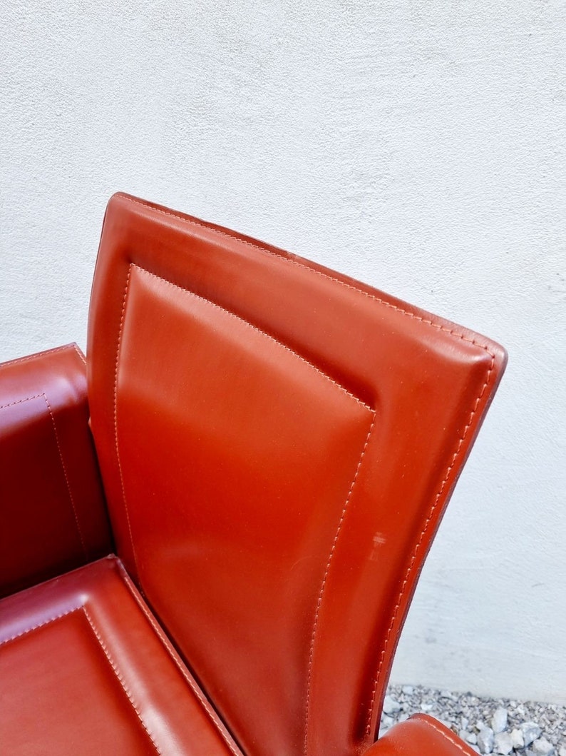 May include: Close-up of a red leather chair with a stitched design. The chair has a high back and a curved seat.