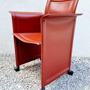 May include: A red leather office chair with a unique design featuring a rectangular back and a curved seat. The chair has four wheels for easy mobility.