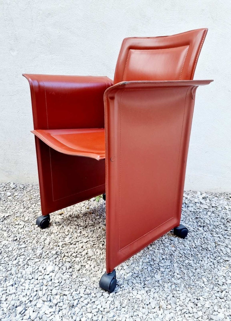 May include: A red leather office chair with a unique design featuring a rectangular back and a curved seat. The chair has four wheels for easy mobility.