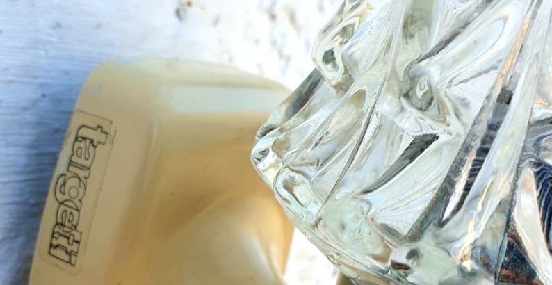 May include: A close-up of a white light fixture with a clear glass shade. The glass shade has a textured, geometric design. The light fixture is labeled "Targetti".