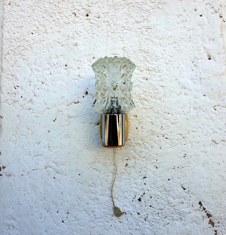 May include: A vintage wall sconce with a clear glass shade featuring a geometric pattern. The sconce has a chrome finish and a gold base.