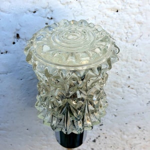 May include: A clear glass lampshade with a textured, faceted design. The lampshade has a round top and a pointed bottom.