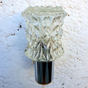 May include: A vintage wall sconce with a clear glass shade featuring a geometric pattern. The sconce has a chrome finish and a gold base.