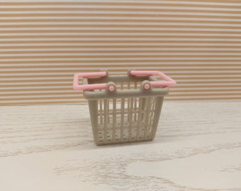 Puede incluir: Una pequeña cesta de la compra de plástico gris con asas rosas. La cesta está vacía.