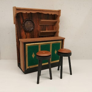 Può includere: Un set da bar in legno con uno schienale verde e oro e due sgabelli da bar neri con sedili marroni.