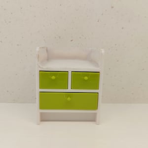 May include: A white dresser with three drawers. The drawers are a bright green color. The dresser is made of wood and has a simple design.