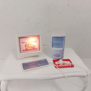 May include: A miniature computer set, including a monitor showing "Welcome to Lundby!" and a keyboard. There's also a computer tower and a mouse on a red and white mousepad. The set is on a white table.
