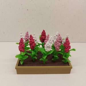 Può includere: Un vaso da fiori in miniatura con fiori rosa e bianchi. Il vaso è in plastica marrone e ha una forma rettangolare.