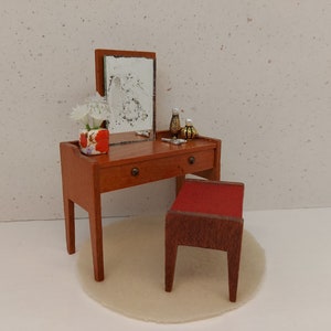 May include: A wooden vanity set with a mirror, a drawer, and a stool. The vanity is decorated with a small bouquet of white flowers in a red and white patterned pot. The stool is upholstered in red fabric.