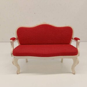 May include: A small, white, ornate, wooden sofa with red upholstery. The sofa has a curved back and scrolled legs.