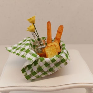 May include: A miniature green and white gingham tablecloth with a small glass jar, two breadsticks, and a few pieces of toast inside.