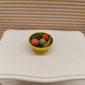 Puede incluir: Un tazón de cerámica amarillo lleno de una variedad de frutas, incluyendo uvas verdes, una manzana roja, una pera verde y un plátano amarillo.