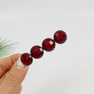 May include: A burgundy hair clip with four round, faceted stones set in gold-toned metal.