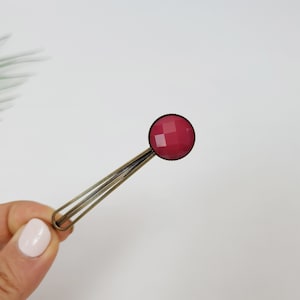 May include: A red, faceted glass cabochon set in a silver tone metal bar clip. The clip is about 2 inches long.