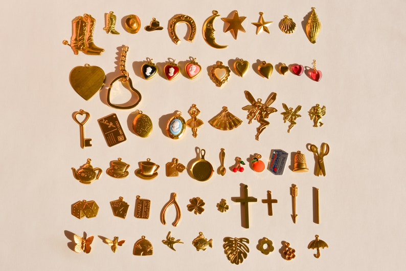 Może przedstawiać: Kolekcja złotych metalowych zawieszek, w tym podkowa, p&oacute;łksiężyc, gwiazda, muszelka, serce, klucz, czajnik, filiżanka, krzyż, motyl, ryba i kwiat.