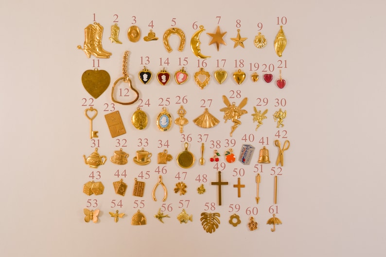 Może przedstawiać: Kolekcja 61 złotych metalowych zawieszek, w tym podkowa, gwiazda, muszla, serce, klucz, czajnik, filiżanka, łyżka, krzyż, motyl, ryba, liść palmy i kwiat. Zawieszki są ułożone w rzędach na białym tle.