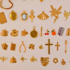 Może przedstawiać: Kolekcja złotych metalowych zawieszek, w tym czajnik, filiżanka do herbaty, kostka do gry, karta do gry, podkowa, koniczyna czteroliścienna, krzyż, strzała, linia, motyl, pszczoła, ul, ptak, ryba, liść monstera, kwiat, grupa kwiat&oacute;w i parasol.