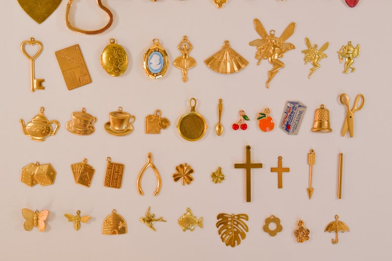 Może przedstawiać: Kolekcja złotych metalowych zawieszek, w tym czajnik, filiżanka do herbaty, kostka do gry, karta do gry, podkowa, koniczyna czteroliścienna, krzyż, strzała, linia, motyl, pszczoła, ul, ptak, ryba, liść monstera, kwiat, grupa kwiat&oacute;w i parasol.