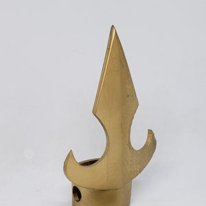 May include: A set of three brass-colored metal components. The largest piece is a decorative spearhead shape with a circular base. A smaller, rectangular rod and a spearhead-shaped piece are also included.