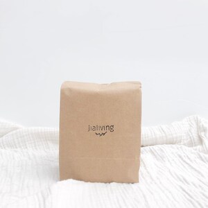 K&ouml;nnte beinhalten: Ein brauner Papierbeutel mit dem Text "jialiving" und einem kleinen Blattdesign, das auf der Vorderseite aufgedruckt ist. Der Beutel liegt auf einer wei&szlig;en Stoffoberfl&auml;che. Der Text "REFILL PACKAGE" ist unter dem Beutel aufgedruckt.