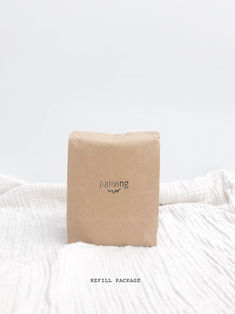 K&ouml;nnte beinhalten: Ein brauner Papierbeutel mit dem Text "jialiving" und einem kleinen Blattdesign, das auf der Vorderseite aufgedruckt ist. Der Beutel liegt auf einer wei&szlig;en Stoffoberfl&auml;che. Der Text "REFILL PACKAGE" ist unter dem Beutel aufgedruckt.