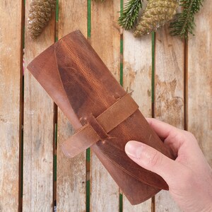 May include: A brown leather roll-up case with a strap closure. The case is made of distressed leather and has a rustic look.