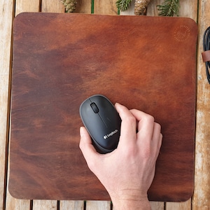 May include: A brown leather mouse pad with a black computer mouse on top. The mouse has the Logitech logo on it.