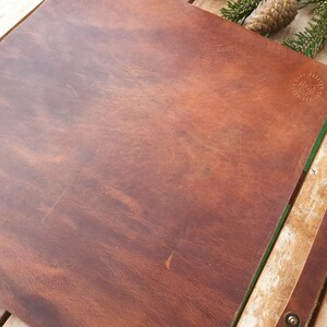 May include: A brown leather desk mat with a subtle embossed design. The mat is on a wooden surface.