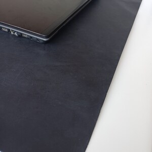 May include: A black laptop computer is sitting on a black leather desk mat. The laptop has the Acer logo on the lid.