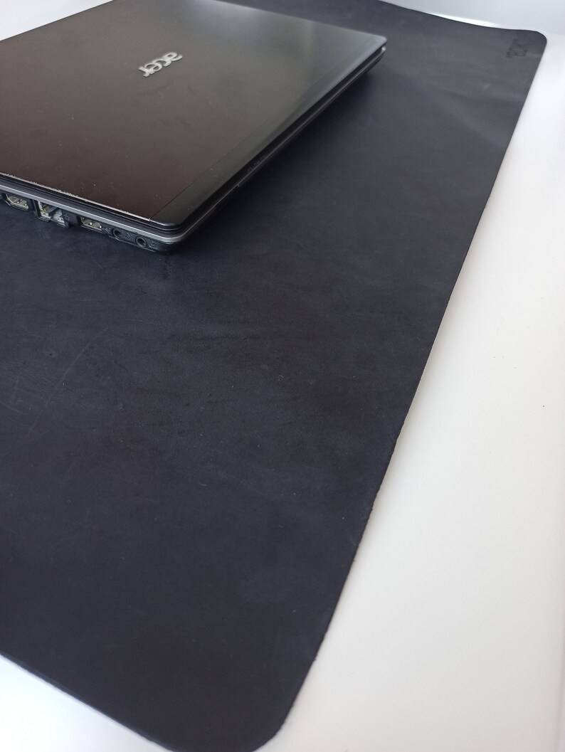 May include: A black laptop computer is sitting on a black leather desk mat. The laptop has the Acer logo on the lid.