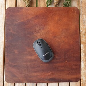 May include: A brown leather mouse pad with a black wireless mouse on top. The mouse has the Logitech logo on it.