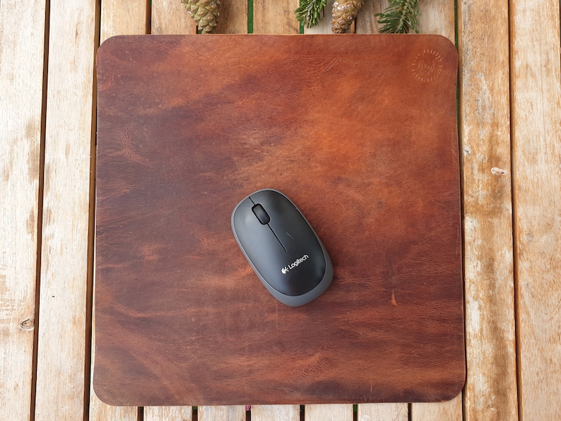May include: A brown leather mouse pad with a black wireless mouse on top. The mouse has the Logitech logo on it.