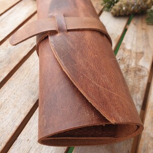 May include: A brown leather roll with a strap and buckle closure. The roll is rolled up and has a worn, distressed look.
