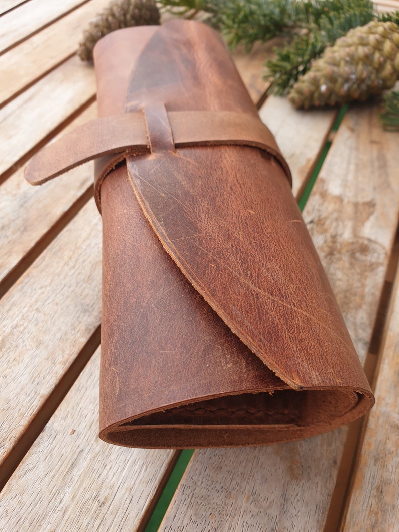 May include: A brown leather roll with a strap and buckle closure. The roll is rolled up and has a worn, distressed look.