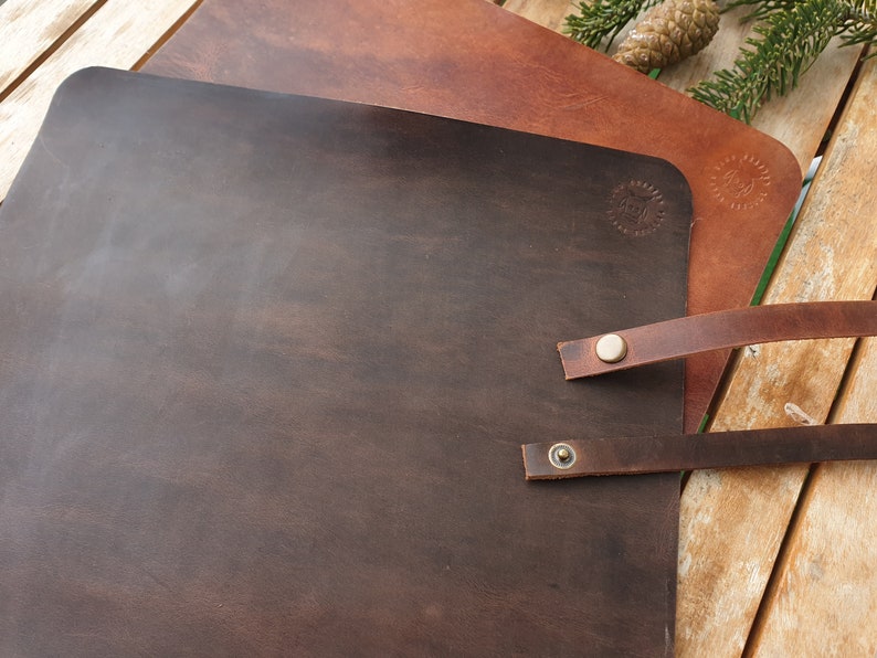 May include: Two leather placemats, one brown and one dark brown, with leather straps and brass rivets. The placemats are on a wooden surface.