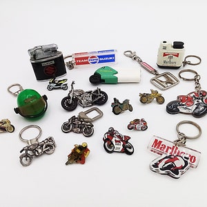 Può includere: Una collezione di portachiavi e accendini a tema motociclistico. I portachiavi presentano motociclette in miniatura, caschi e un logo Marlboro verde e rosso. Gli accendini sono argentati e neri con le parole "Suzuki" e "Marlboro" stampate su di essi.