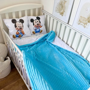 May include: A white crib with a blue and white crib bedding set featuring a Mickey Mouse design. The crib is decorated with two framed pictures of a giraffe and a crib.