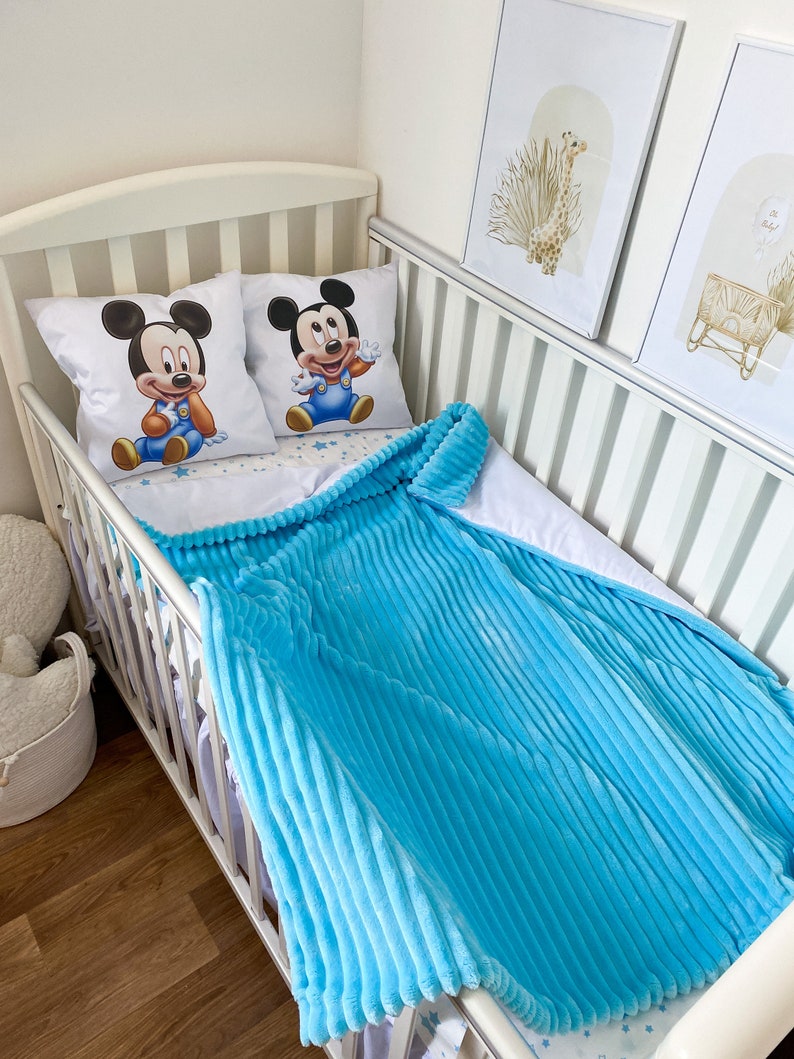 May include: A white crib with a blue and white crib bedding set featuring a Mickey Mouse design. The crib is decorated with two framed pictures of a giraffe and a crib.