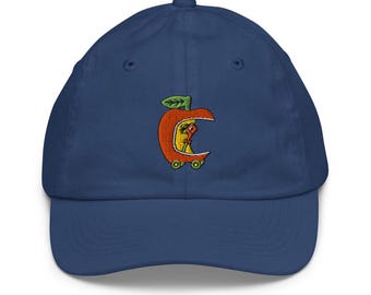 May include: A navy blue baseball cap with a curved brim. The cap features an embroidered orange apple design with a worm inside. The apple has a green leaf and is on a yellow background. The cap has a button on top.