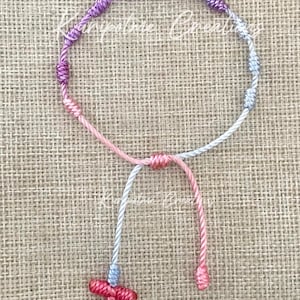 May include: A pink, purple, and silver braided rosary bracelet with a silver charm and a red cross.